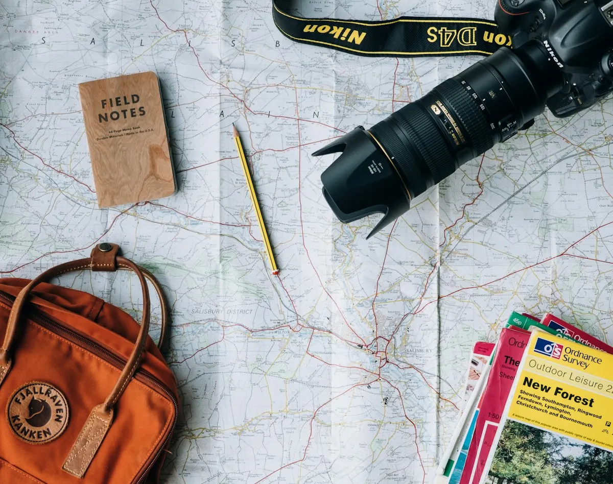 Mapa, câmera e caderno sobre a mesa durante o planejamento de uma viagem